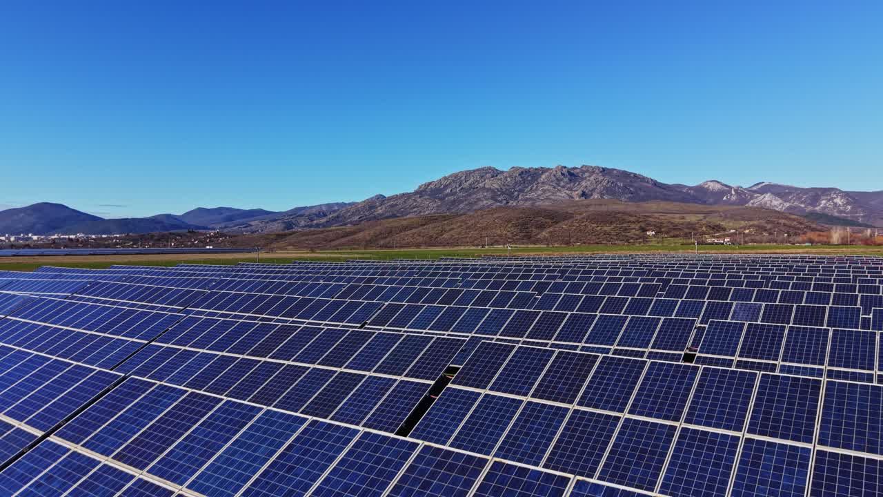 Solpaneler dækker jorden under en klar, blå himmel nær bjergene om dagen