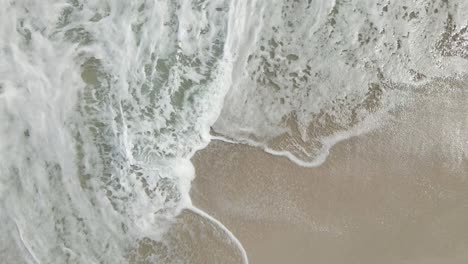 still drone shot above beach sand as ocean water wash over it