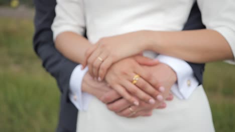 newlywed bride and groom hug as their hand touches each other with their wedding rings - the couple's hands caress each other