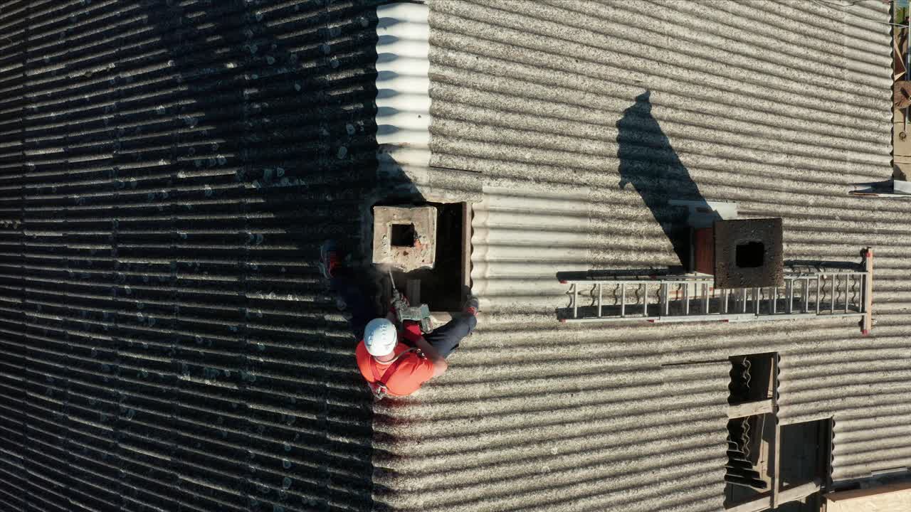 Aeriel shot pulling in on a construction worker operating a drill on a roof in the afternoon