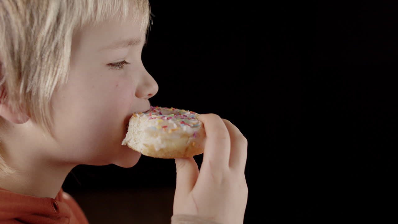 Boy bites into delicious sweet glazed donut dessert, close-up profile