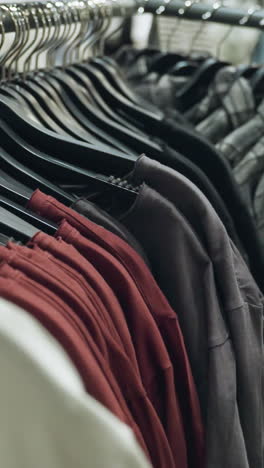 kledingwinkel, vastgelegd met een handheld camera, met een close-up van verschillende kleding op hangers, waaronder shirts, jassen en blouses