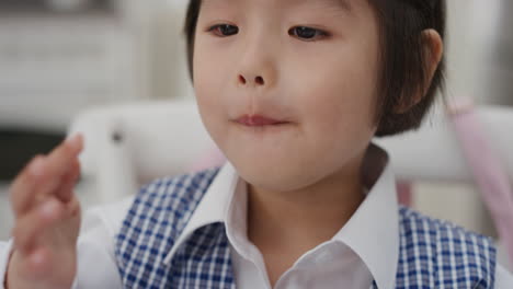 cute little asian girl eating breakfast enjoying cereal in kitchen getting ready wearing school uniform 4k