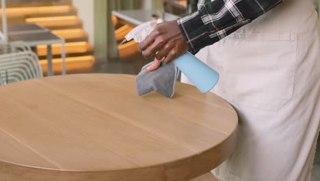 waiter cleaning coffe shop table with disinfectant spray and rag