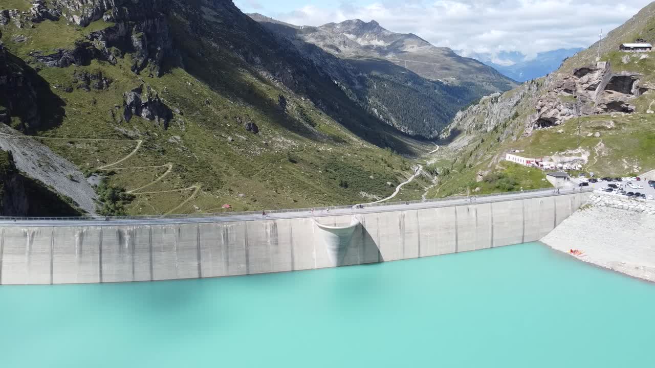 vuelo de drones lateralmente a lo largo de la pared de la presa de la asombrosa pared de la presa del lago de moiry con un paisaje de libro de imágenes de los alpes suizos en el fondo, buen clima soleado