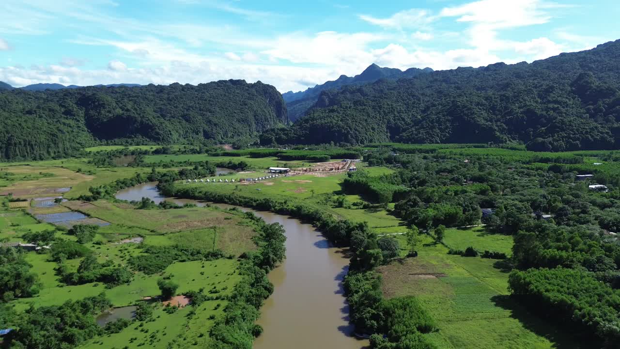 Smooth zoom in towards a winding river surrounded by rice fields and karst limestone mountains in Phong Nha. Bright daylight and clear sky