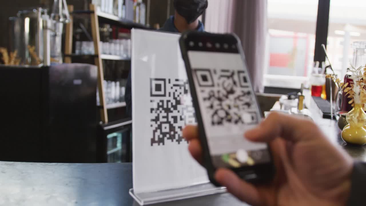 African american woman in face mask serving customer reading qr code with smartphone at cafe bar