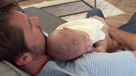 father sitting on sofa holding sleeping baby son