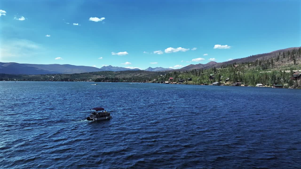 Summer pontoon yacht boating at Grand Lake Granby aerial drone Colorado Rocky Mountains National Park entrance breeze on body of water sunny morning daytime clouds lake homes forward motion