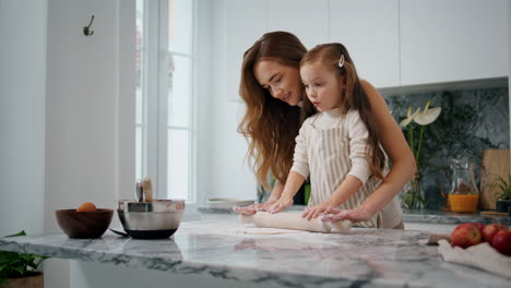 Lächelnde-Mutter-Bringt-Tochter-Das-Backen-In-Der-Küche-Bei.-Kind-Rollt-Teig