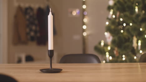 Die-Kamera-Konzentriert-Sich-Auf-Die-Hände-Eines-Kindes,-Die-Ein-Milchglas-Und-Einen-Teller-Voller-Kekse-Auf-Einen-Leeren-Tisch-Mit-Zwei-Kerzen-In-Einem-Mit-Einem-Weihnachtsbaum-Geschmückten-Raum-Stellen