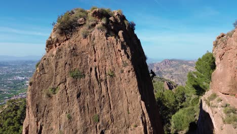 Man-rock-climbing-aerial-view-of-sportsman-rapelling-mountain-in-La-Panocha,-el-Valle-Murcia,-Spain-woman-rapel-down-a-mountain-climbing-a-big-rock