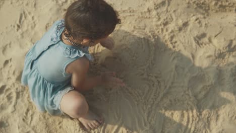 top-down-view-of-young-toddler-playing-in-sand-at-beach-with-sun-rays-behind