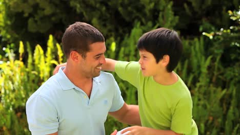 hijo dándole a su padre una pelota de fútbol y un abrazo
