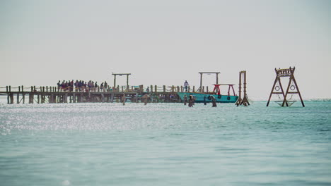 Zeitraffer-Eines-Piers-Im-Meer-Mit-Einem-Spielplatz-Im-Wasser,-Wo-Touristen-Spazieren-Gehen-Und-Boote-Anlegen