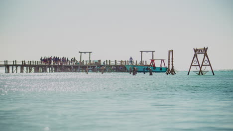lapso de tiempo de un muelle en el océano con un parque infantil en el agua y donde los turistas caminan y los barcos amarran