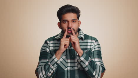 young indian man presses finger to lips makes silence gesture sign do not tells secret stop gossip