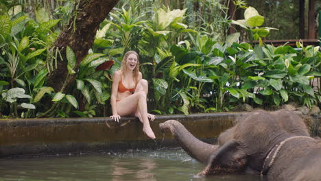 travel woman playing with elephant in zoo spraying water having fun on exotic vacation in tropical forest sanctuary