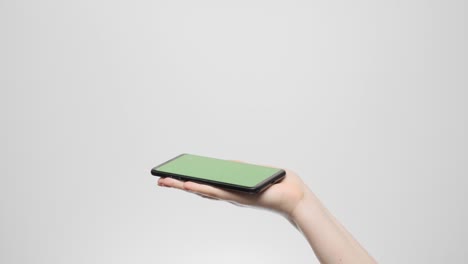 phone with a green screen in a woman's hand on a gray background.