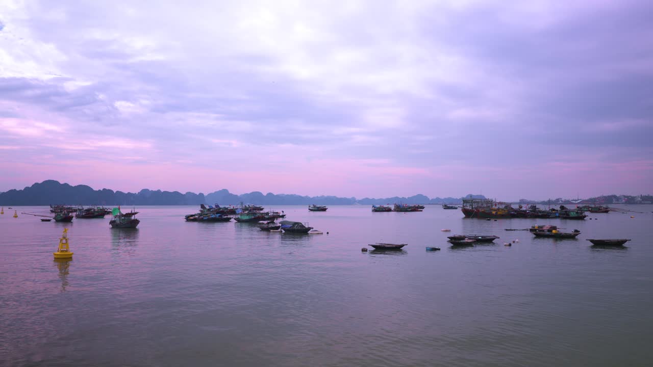 Majestic limestone karsts silhouette against a lavender-tinted sky while traditional Vietnamese fishing trawlers drift serenely on the tranquil waters of Ha Long Bay at twilight
