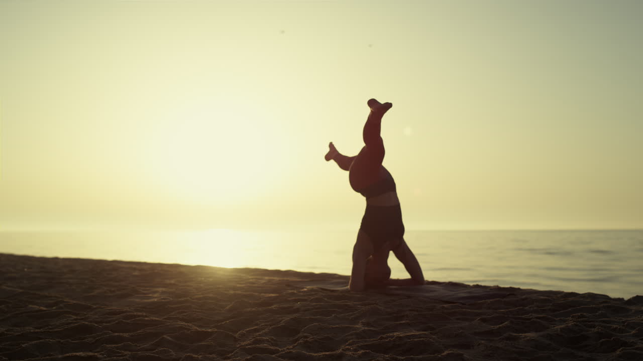 Yoga yapan kadın gün batımında baş duruşu yapıyor. Güçlü genç kadın ters duruşta.