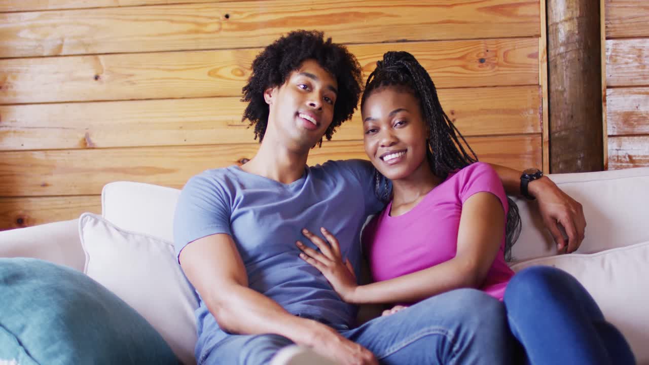 Ritratto di felice coppia afroamericana seduta sul divano in baita di legno, slow motion