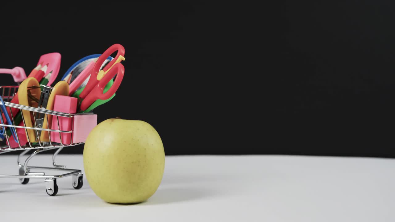 cerrar el carrito de compras con artículos escolares y manzana con espacio de copia en fondo negro