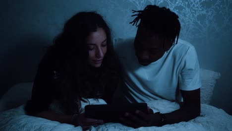 couple sitting up in bed at night watching a tablet device