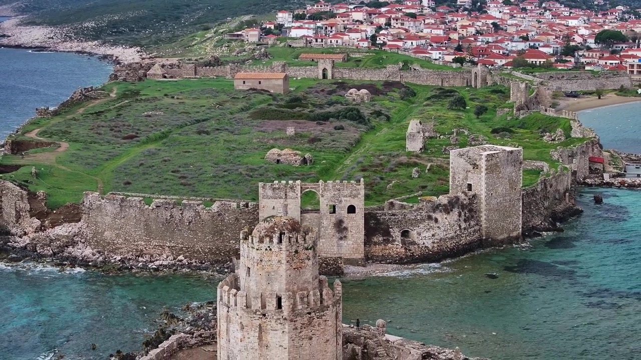 Ripresa aerea con drone dall'alto che mostra le mura di fortificazione in pietra del Castello di Methoni, campi verdi all'interno della fortezza e la torre ottagonale di Bourtzi con la città costiera in Messenia, Peloponneso, Grecia.