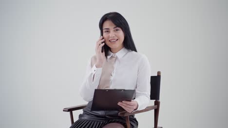 portrait of dark-haired woman talking the phone. beautiful young business woman sitting in the chair and holding black folder in the studio.