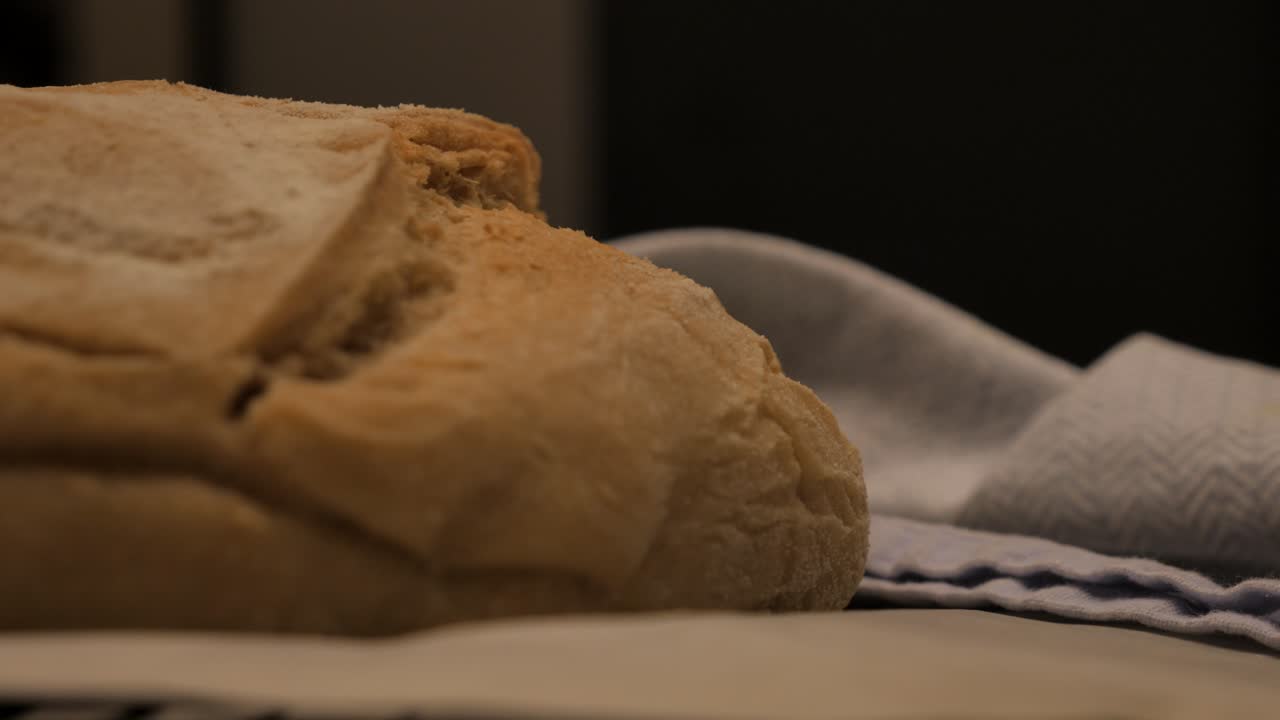 Slow motion pan towards freshly baked loaf of sour dough bread topped with flour sitting on kitchen bench with tea towel and tray, low depth of field