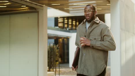 man walking outdoors with coffee and folder