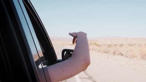 female passenger with arm out of car window on desert drive