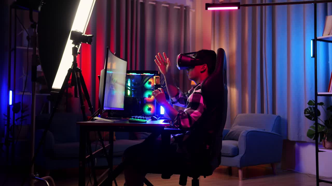 Side View Of Asian Boy Streamer Playing Game Experience Virtual Reality In Futuristic Goggles. Player Touching Air Panel. Personal Computer On Desk Illuminated By Rgb Led Strip Light