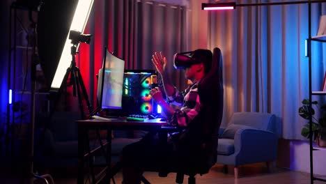 side view of asian boy streamer playing game experience virtual reality in futuristic goggles. player touching air panel. personal computer on desk illuminated by rgb led strip light