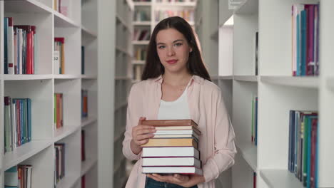joven profesor con pila de folio en la biblioteca de la universidad. bibliotecario feliz recomienda literatura para leer en la librería. dama bonita con colección de libros