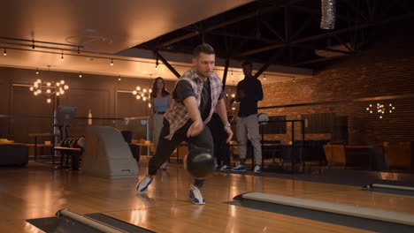 a man in a bowling alley throws a ball on the track and knocks out a shot in slow motion and jumps and dances for joy. friends fans. a group of multi-ethnic friends play bowling together.