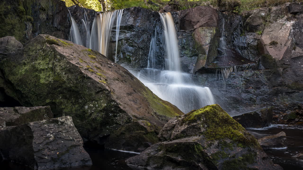 Zeitraffer eines lokalen Wasserfalls in einer ländlichen Waldlandschaft Irlands an einem sonnigen Sommertag