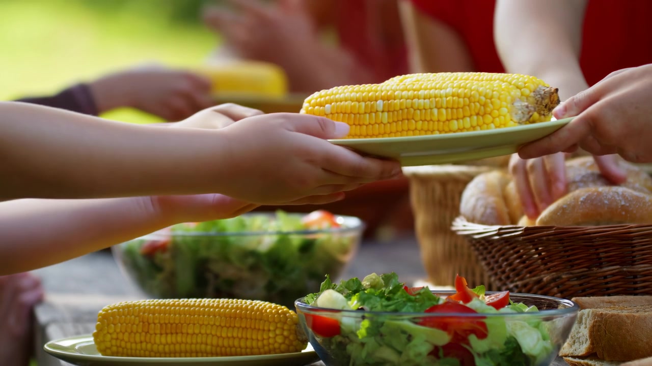 Outdoor Picnic Table With Corn Passed Between Hands, Children Sharing Plate During Family Backyard Lunch,