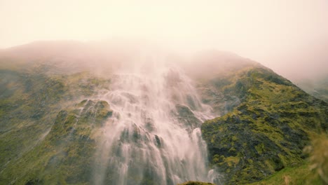 Serene-waterfall-with-clean-spring-water-flowing-down-a-cliff-with-rocks-covered-in-moss