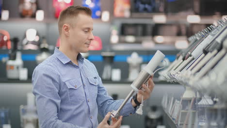 In-the-appliances-store,-a-man-in-a-shirt-chooses-a-blender-to-buy-by-viewing-and-holding-the-device.