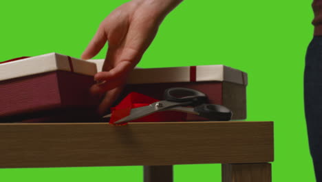 primer plano de un hombre envolviendo regalos en cajas decoradas con cinta en una mesa disparada contra una pantalla verde 2