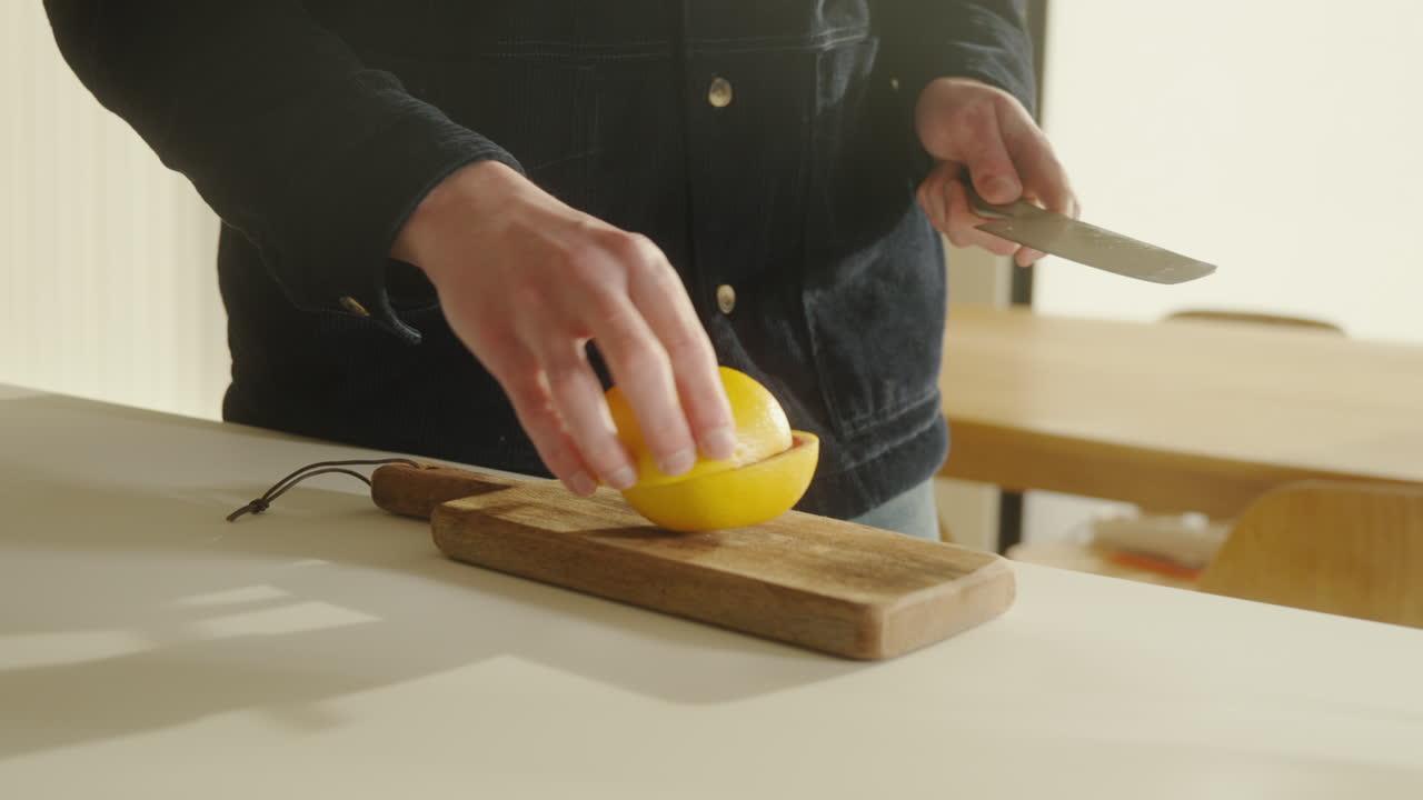 Male cutting grapefruit in halfs on a wooden cutting board with sharp knife in the kitchen at home 4k