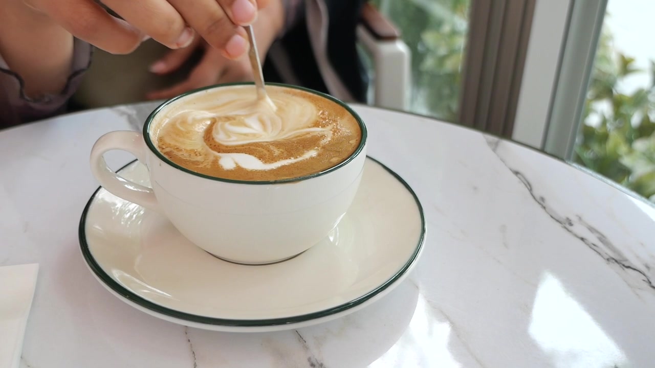 Persona che mescola la latte art in una tazza di caffè bianca