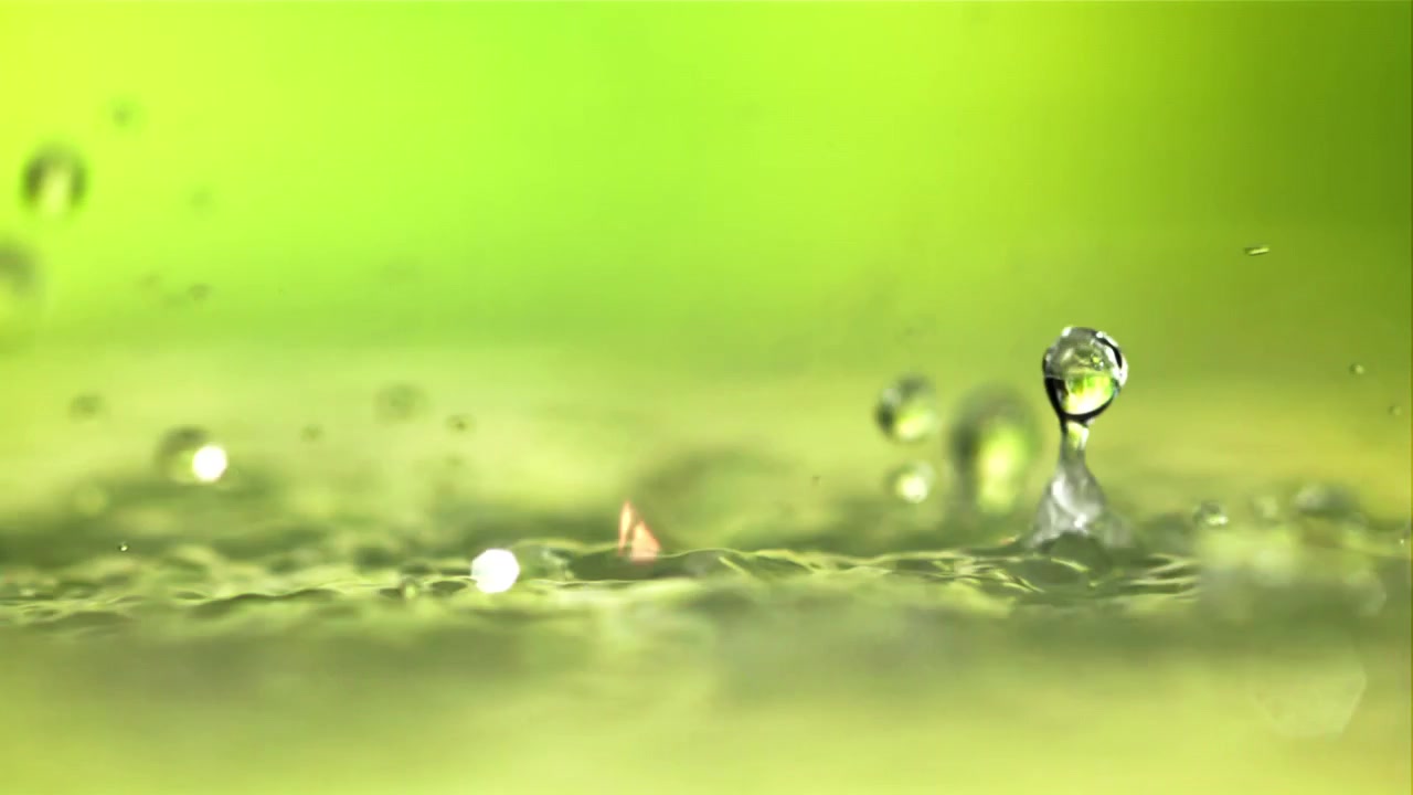 Wassertropfen spritzen in Zeitlupe auf eine grüne Flüssigkeitsoberfläche.