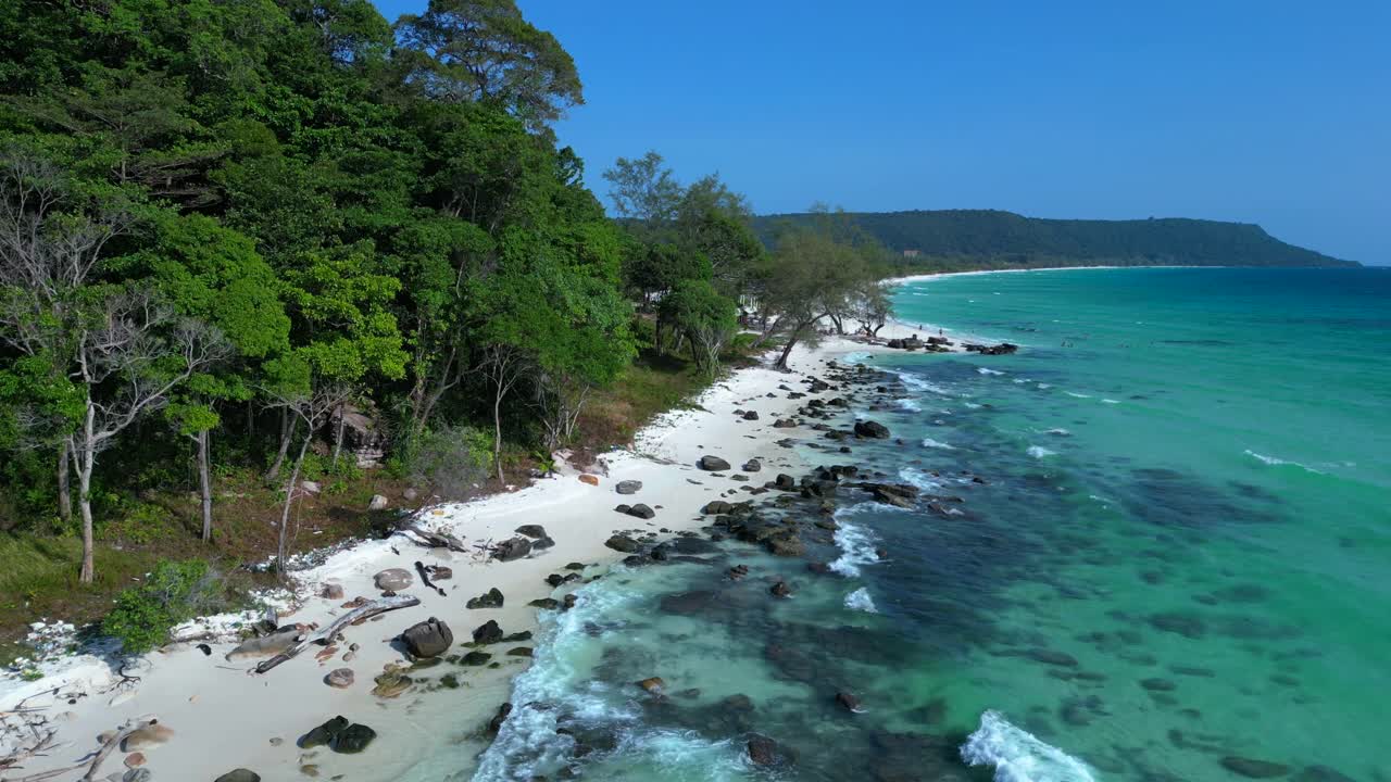 Black Stones in turquoise water gently washing the white sand beach of Koh Rong island, cambodia, on a sunny day with clear blue sky. Fabulous aerial view flight panorama overview drone