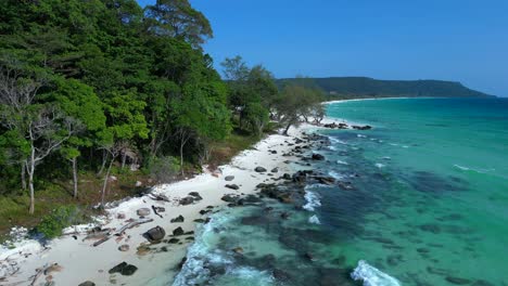 black stones in turquoise water gently washing the white sand beach of koh rong island, cambodia, on a sunny day with clear blue sky. fabulous aerial view flight panorama overview drone