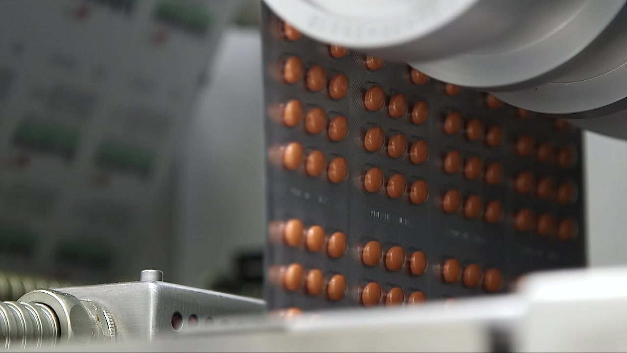 Close-up of pharmaceutical blister packs filled with tablets moving through an automated packaging machine during medicine production in a modern pharmaceutical factory.