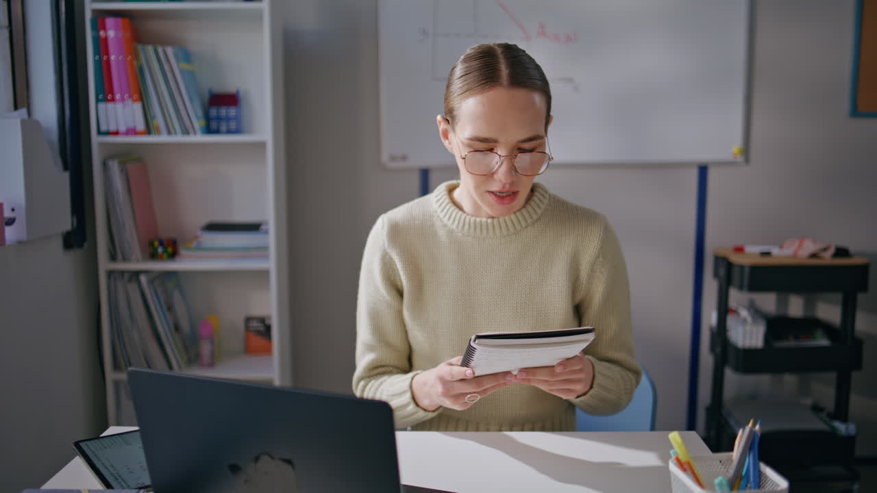 Young teacher wearing glasses looking notebook at school closeup. Woman working