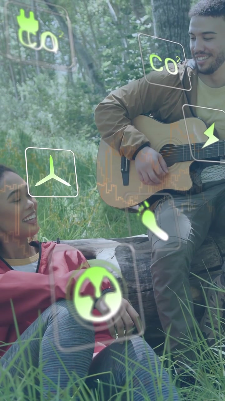 Video verticale: Uomo che strimpella la chitarra su un tronco, donna che sorride e crea un legame, con icone di energia che appaiono sopra la coppia.